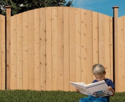 Child reading a book in front of wood privacy fence