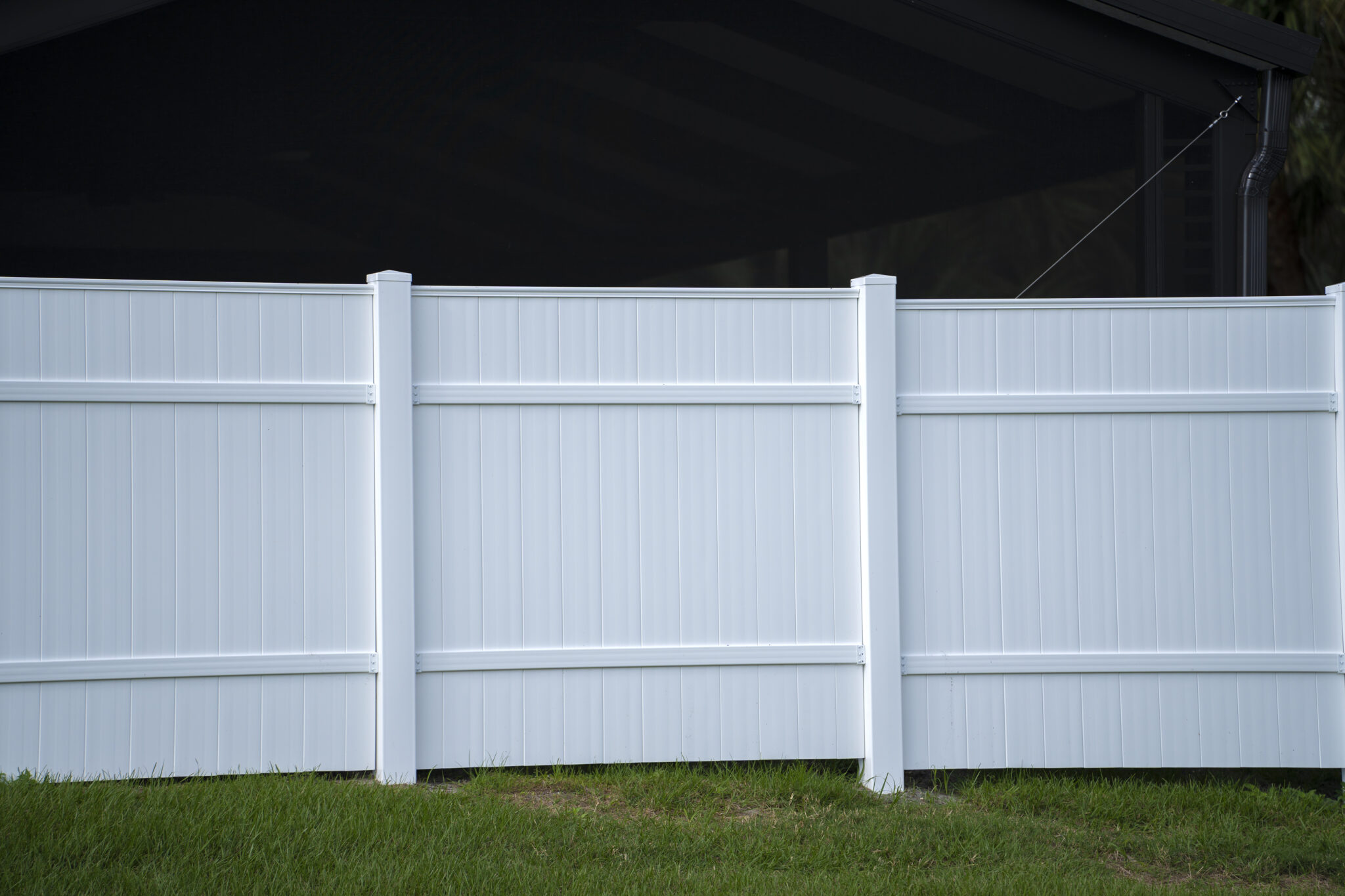 White vinyl picket fence on green lawn surrounding property grounds for backyard protection and privacy.