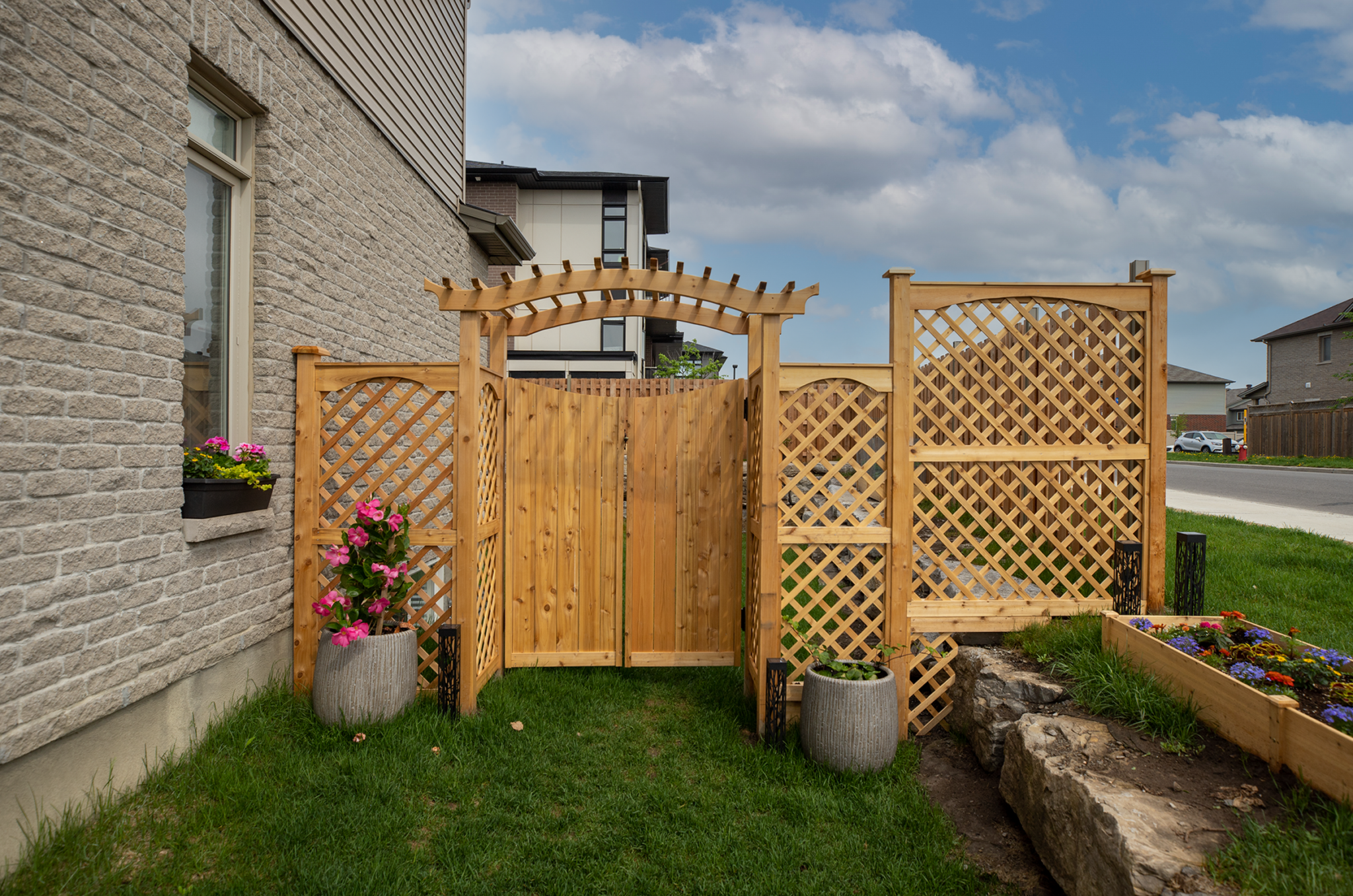 Wooden backyard gate with decorative arbor integrated into a privacy fence and garden landscaping.