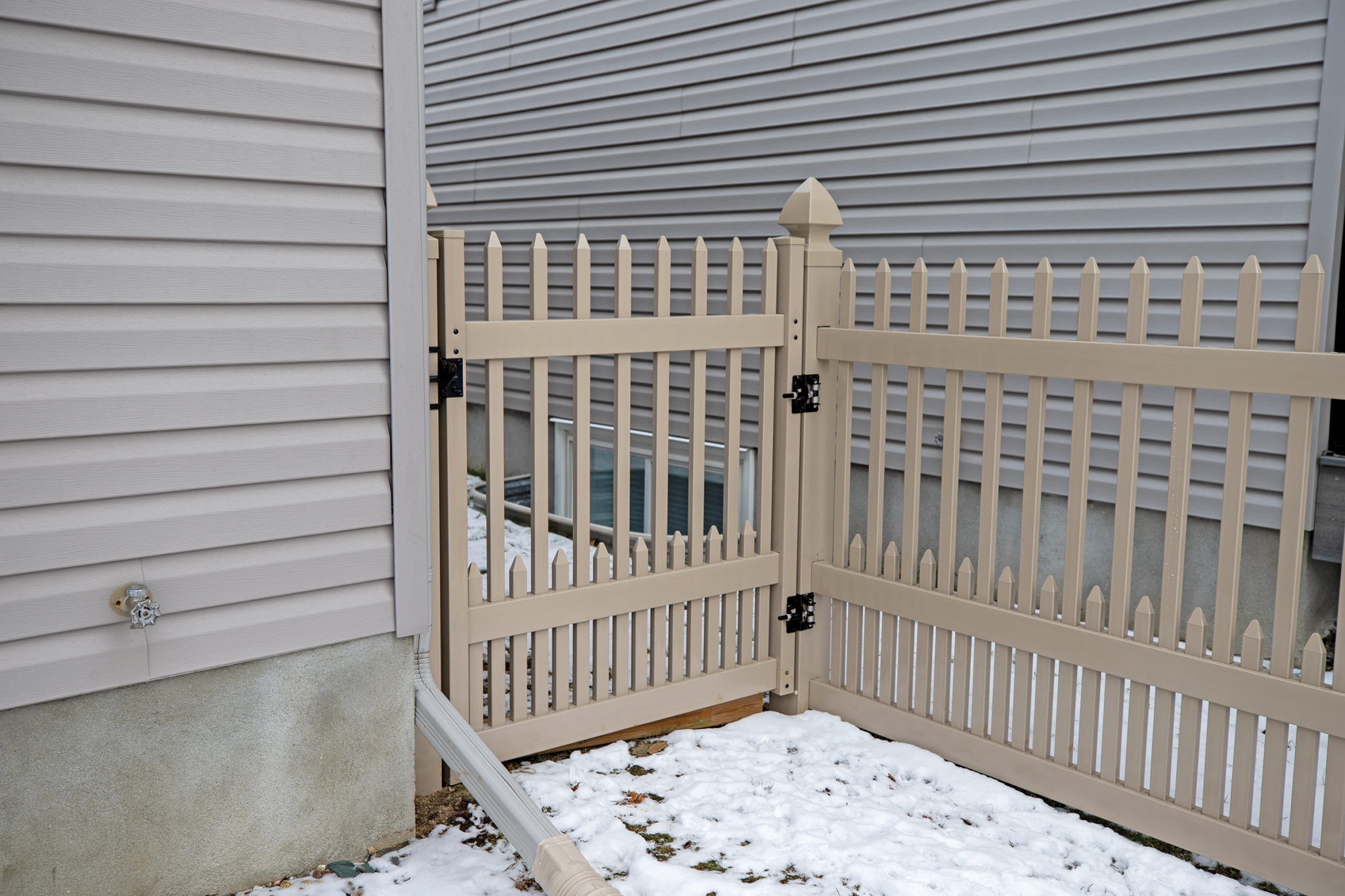 Beige vinyl fence gate installed beside a home providing durable and low-maintenance backyard access.