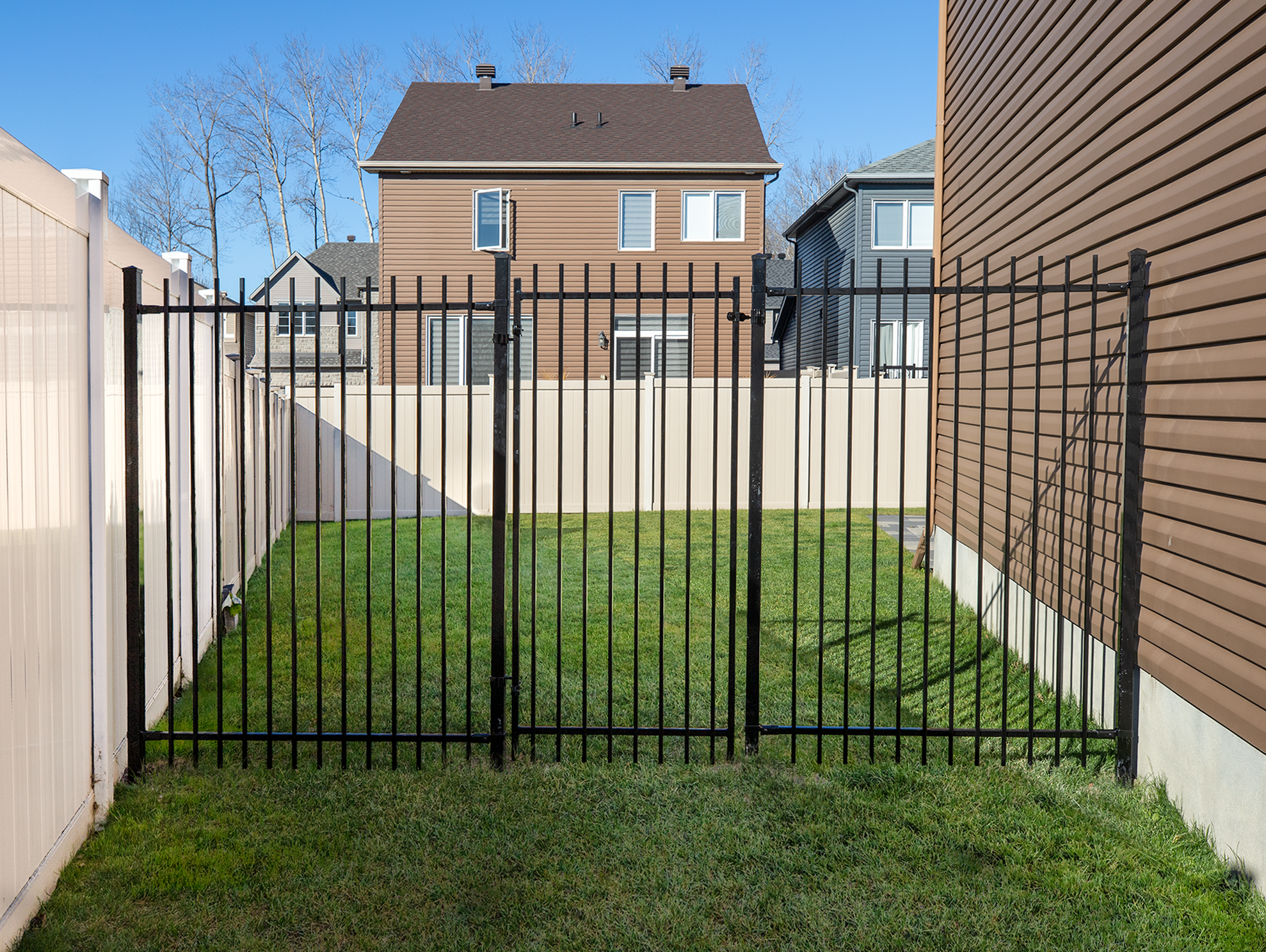Black metal double gate installed within a backyard fence allowing wide access between residential properties.