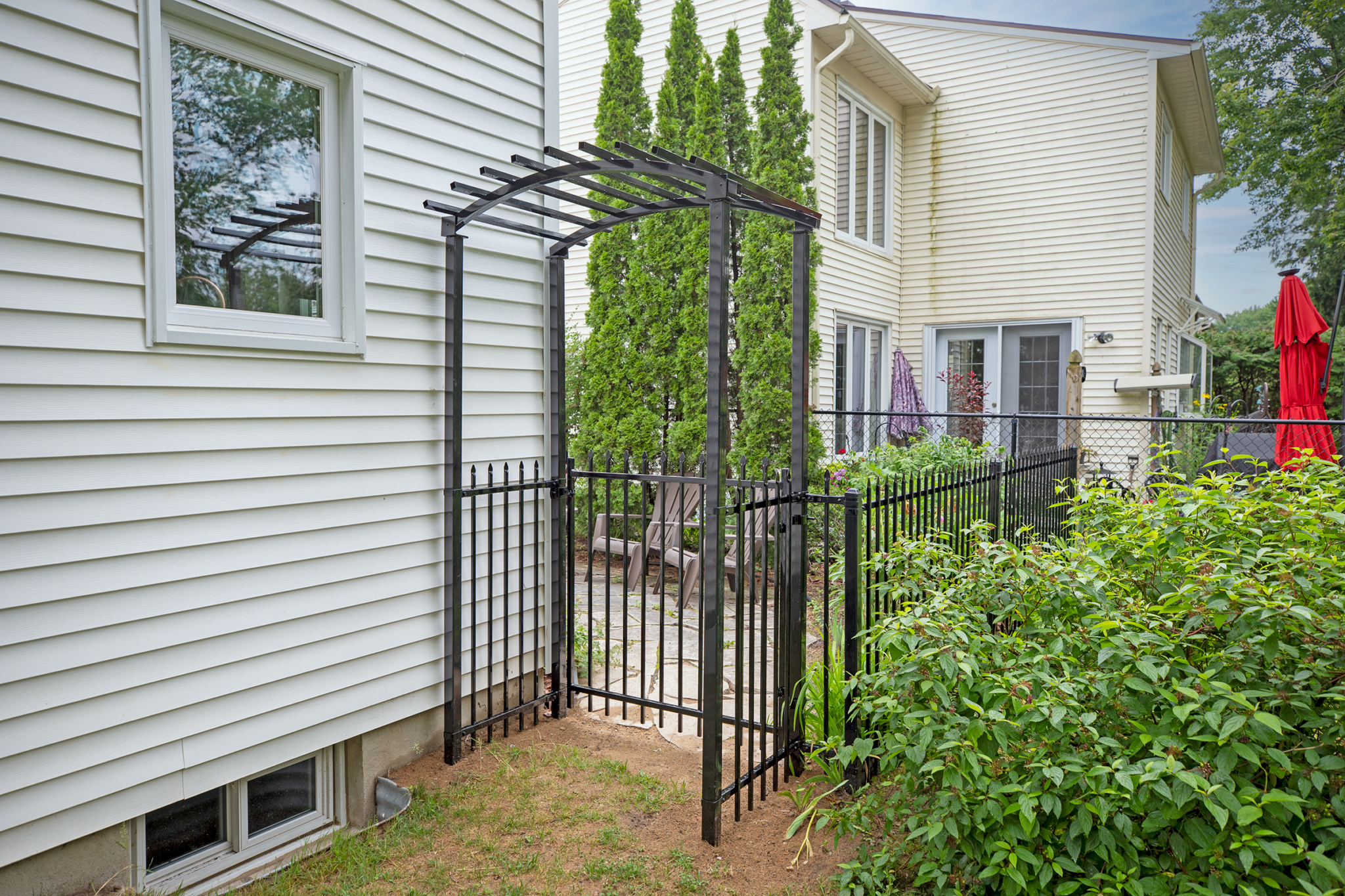 Black metal side yard gate installed between a house and fence providing secure backyard access.
