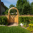 Decorative wooden garden gate with arched arbor integrated into a lattice privacy fence in a landscaped residential backyard.